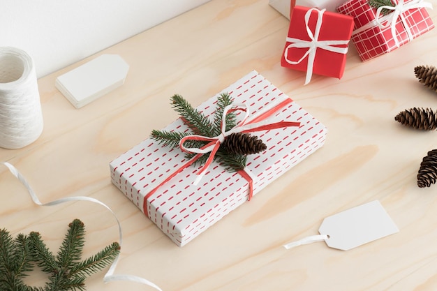 White christmas gifts surrounded with pine cones leaves and twine on a wooden table