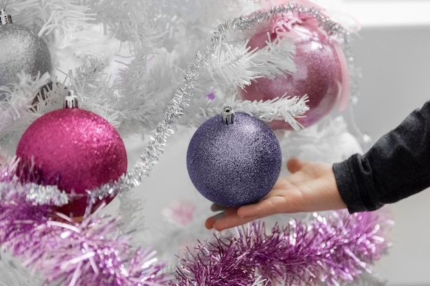 White Christmas tree Childs hand touches balls on the Christmas tree Closeup