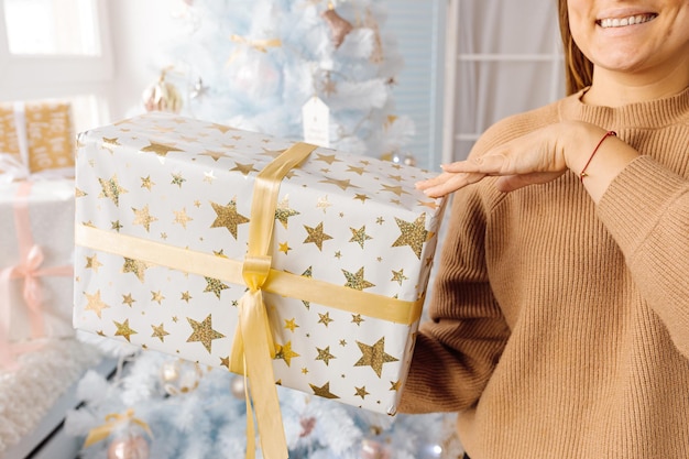 흰색 크리스마스 트리는 은색 황금색 분홍색 크리스마스 공과 반짝이는 요정 흰색 파란색 나뭇가지, 장식용 조명, 복사 공간에 아름다운 유리 공으로 장식되어 있습니다. 사진, 손을 잡고 선물 상자
