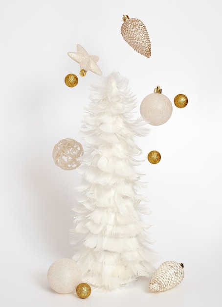 白いクリスマスツリーと白い背景の上の空飛ぶ装飾。クリスマス作文。現代のクリスマスの背景。