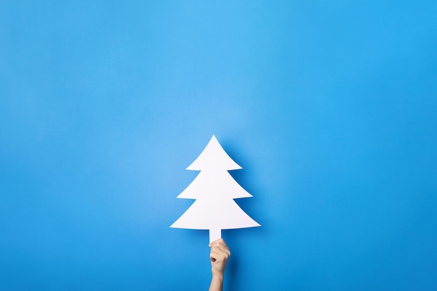 White christmas tree in hand over blue background, merry christmas concept