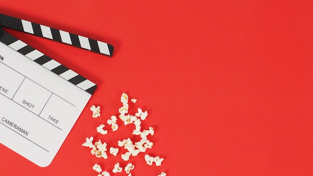 White Clapper board or movie slate and popcorn on a red background.