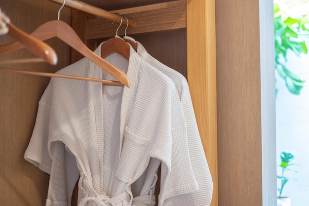 white clean bathrobe hanging in wooden wardrobe at luxury hotel or home relax and travel concept