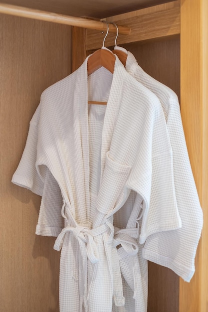 고급 호텔 또는 홈 휴식 및 여행 컨셉의 나무 옷장에 흰색 깨끗한 목욕 가운이 걸려 있습니다.