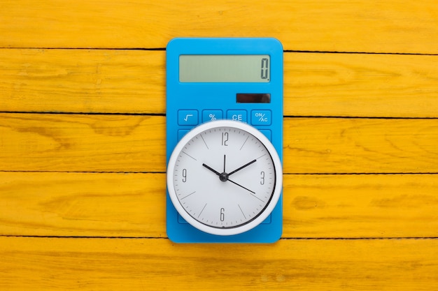 White clock and calculator on yellow wooden surface. minimalistic studio shot. top view