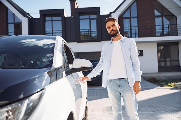 Photo in white clothes young stylish man is with electric car at daytime