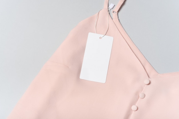 White clothing tag, label blank mockup template. On a premium cotton pink blouse on gray background