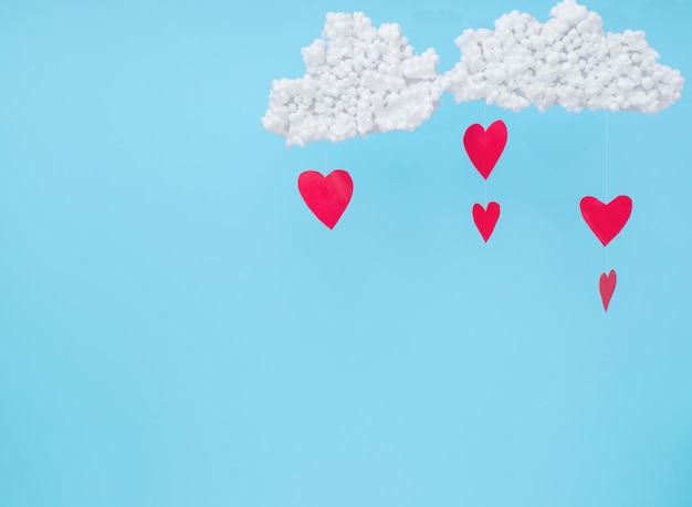 White clouds and red paper hearts in the form of rain on a blue background