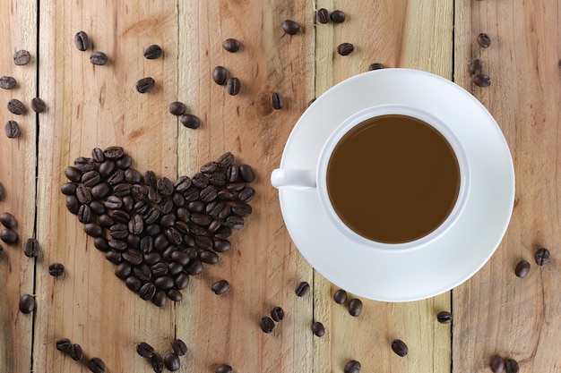 Белая чашка кофе и кофейные бобы имеют форму сердца.