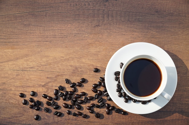 Tazza di caffè bianco e chicchi di caffè sul tavolo scrivania in legno.