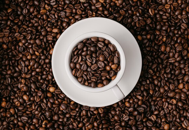 White coffee cup lies in roasted coffee beans