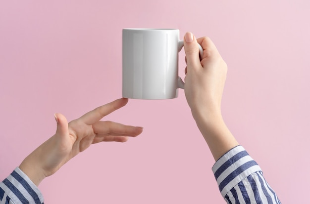 white coffee cup or mug in female hands on pink