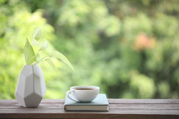 White coffee cup and notebook with devil ivy plant on wooden\
table