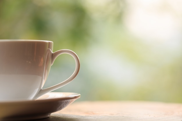 White coffee cup on table in garden with blur light bokeh