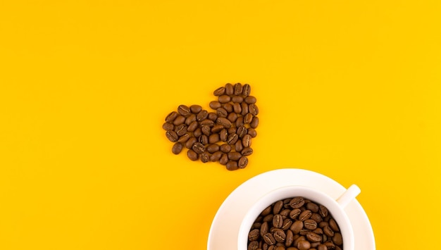 White coffee cup with beans in shape of heart Yellow background Copy space