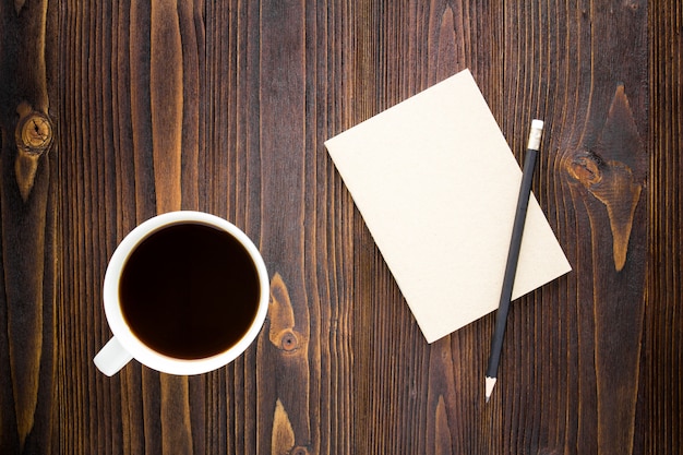 White coffee cup with black coffee ,notebook and pencil on wooden table.