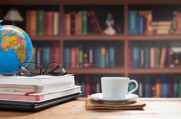 White coffee cup with books stacked and black laptop on wooden table in home office room