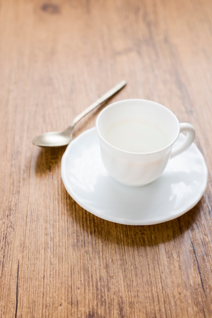 White coffee cup with coffee stains next to spoon and on wooden background