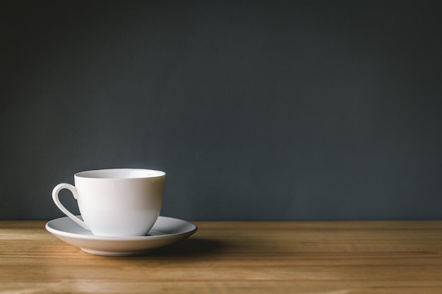 灰色の背景を持つ木製の机の上の白いコーヒーカップ