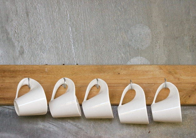 White coffee cups hanging on wood panel with cement wall background.