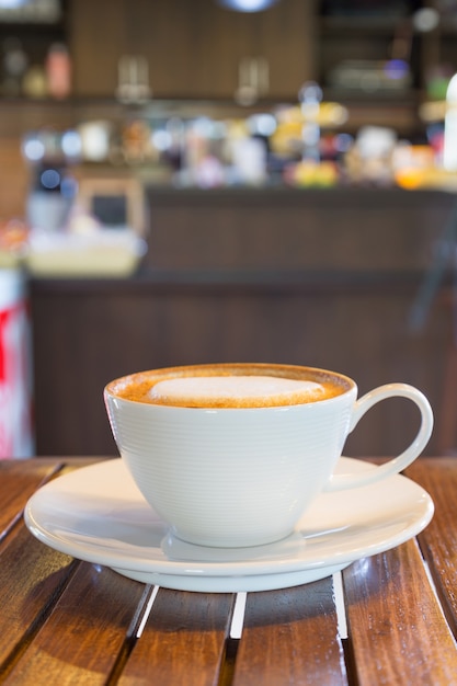 White coffee mug is placed on a wooden table in a coffee shop.