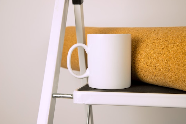 White coffee mug mockup with cork coating roll and stepladder