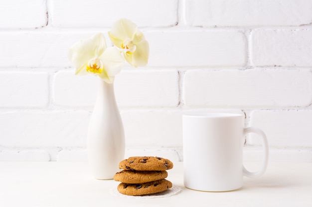 White coffee mug mockup with soft yellow orchid in vase and cookies