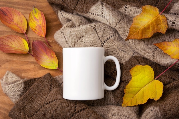 Tazza da caffè bianca mockup rustico con coperta lavorata a maglia e foglie rosse gialle autunnali. tazza vuota mock up per la promozione del design, modello in stile