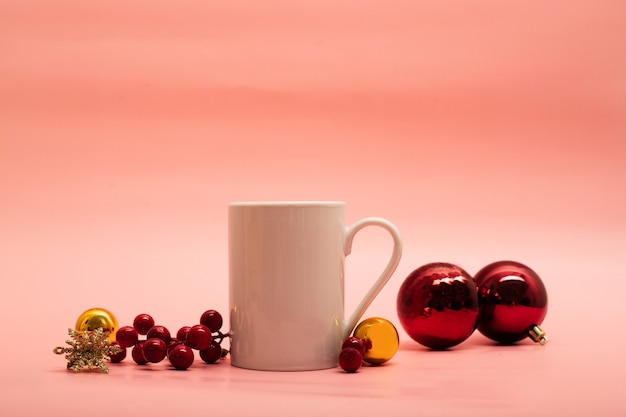 White coffee mug with christmas ornaments around it on pink background