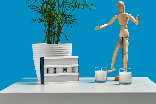 White coffee table with green flower in pot two candles wooden figurine of human and decor element with inscription home Blue background Interior design Close up copy space