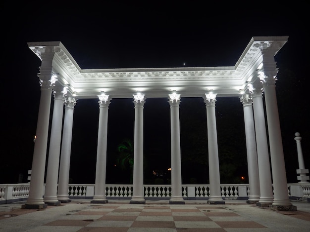 Белая колоннада в темноте Белые колонны в свете прожекторов Элемент архитектурного ансамбля в городском парке