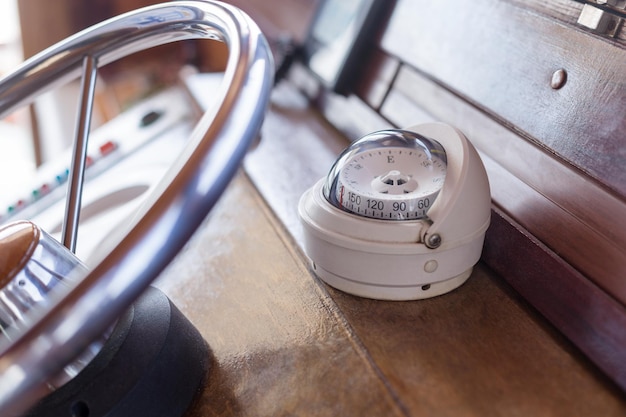 White compass on old ship next to a metal steering wheel closeup