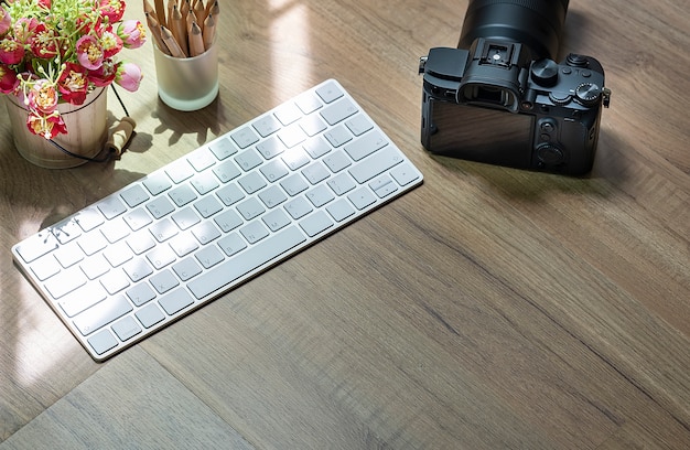 White computer keyboard and digital camera on wooden table