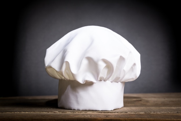 White cooks cap on table over drak background.
