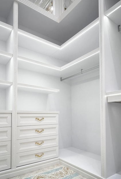 White corner wardrobe section with empty rack and led illumination on shelves in spacious walk-in cl