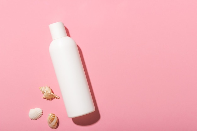 White cosmetic bottle with face cream or lotion and telana against a pink background with seashells Sun cream summer cosmetics