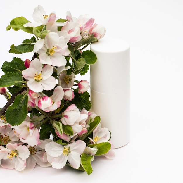 White cosmetic bottle with pear flowers on a white background. Natural organic cosmetics concept.