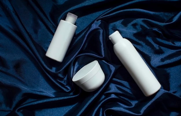 White cosmetic bottles on a blue fabric drapery, a model of cosmetic tubes, a natural spa cosmetic product, a container for liquid cosmetics, shampoo, a place for inscriptions and a brand logo.