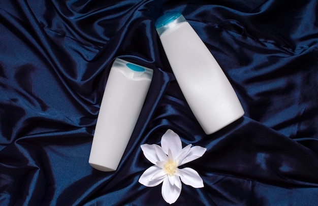 White cosmetic bottles on a blue fabric drapery, a model of cosmetic tubes, a natural spa cosmetic product, a container for liquid cosmetics, shampoo, a place for inscriptions and a brand logo.