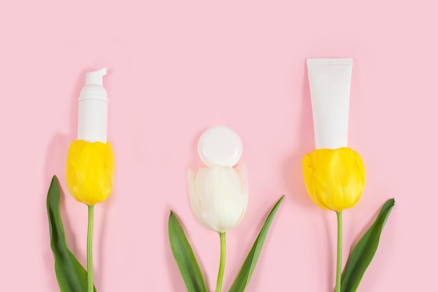 White cosmetic bottles containers on yelolow and white tulips flowers