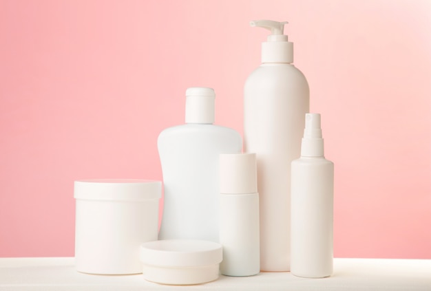 White cosmetic bottles on pink wall. Top view