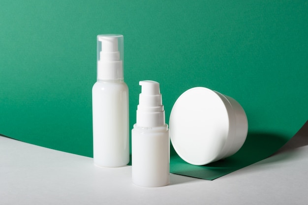 White cosmetic bottles with cream, face mask on a green background. Mockup of a moisturizer.