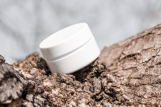 White cosmetic jar on tree bark