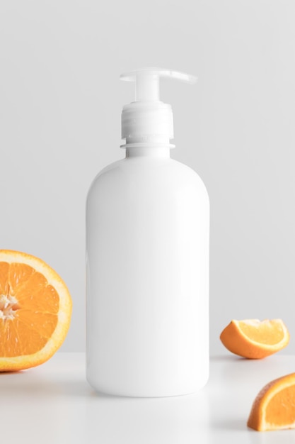 White cosmetic liquid soap dispenser bottle mockup with oranges on a white table