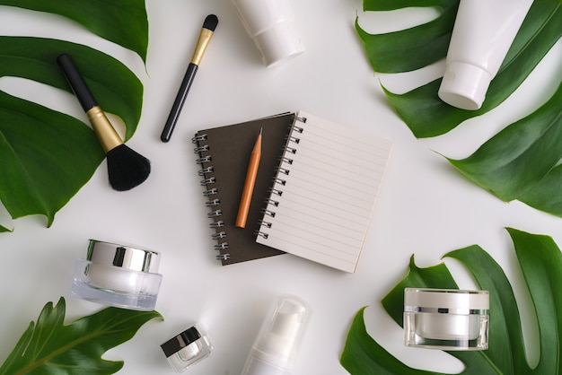 White cosmetic products and green leaves on white background