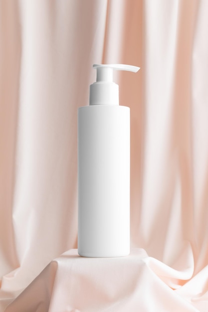 Макет бутылки белого косметического дозатора шампуня на нежно-розовой ткани