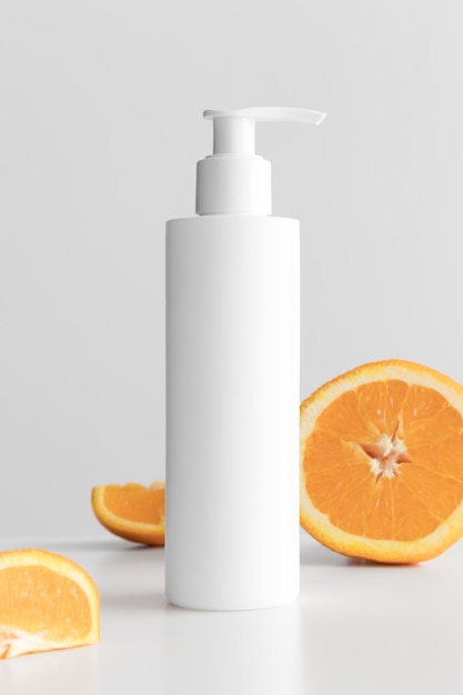 White cosmetic shampoo dispenser bottle mockup with oranges on a white table