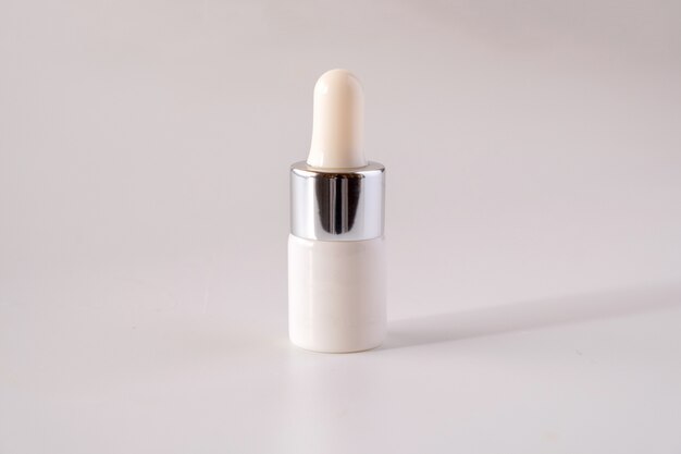 Белая косметическая бутылка-капельница на белой поверхности