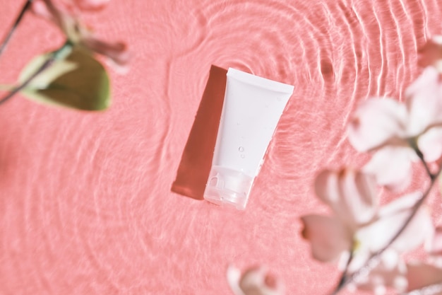 White cosmetic tube on the pink water surface Blank label for branding mockup Flat lay top view