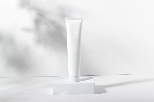 Photo white cosmetic tube on a stand with leaves and shadows toothpaste face and body cream female cosmetic tube with skin care product organic cosmetics copy space